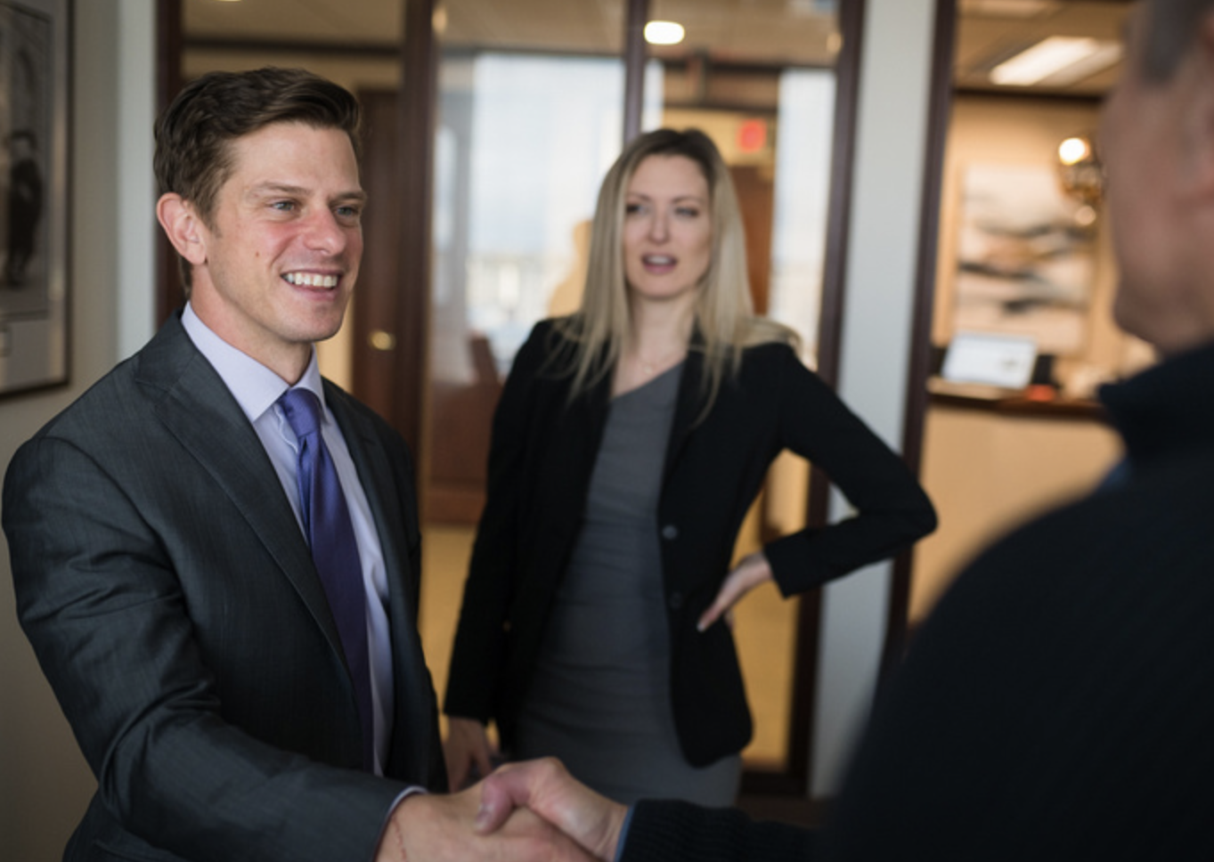 Advisor in a suit smiling and shaking hands with a client in an office